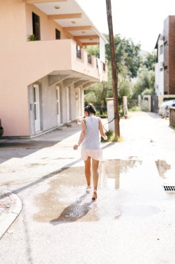 Genç bir kadın asfalttaki su birikintilerinde yalın ayak yürüyor. Arkadan bak. Yüksek kalite fotoğraf