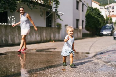 Küçük kız gülüyor ve annesinden su birikintilerinde kaçıyor. Yüksek kalite fotoğraf