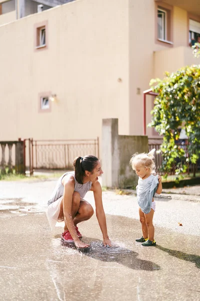 Mom splashes water from a puddle with her hands near a little girl. High quality photo