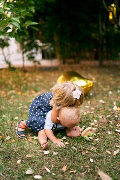 Little girl hugs from behind a small boy sitting on a green lawn. High quality photo