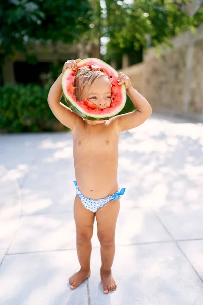 Küçük kız kafasına koyarak yuvarlak bir karpuz parçası yer. Yüksek kalite fotoğraf