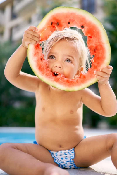 Küçük kız kafasının üstünde tutarak bir karpuzu kemiriyor. Yüksek kalite fotoğraf