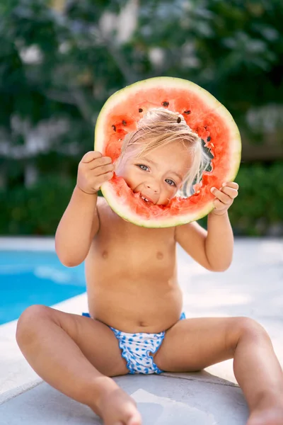 Küçük kız bir karpuz parçasında bir delik açar ve onu yüzüne yaklaştırır. Yüksek kalite fotoğraf