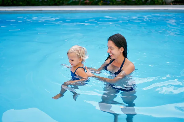 Gülümseyen anne havuzda turkuaz suda küçük bir kız taşıyor. Yüksek kalite fotoğraf