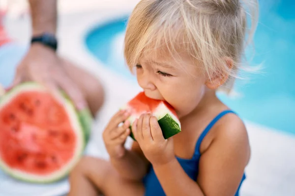 Mayo giymiş küçük bir kız havuz kenarında turkuaz suyla karpuz yiyor. Portre. Yüksek kalite fotoğraf