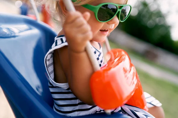 Güneş gözlüklü küçük kız salıncakta sallanıyor. Yan görüş. Yüksek kalite fotoğraf