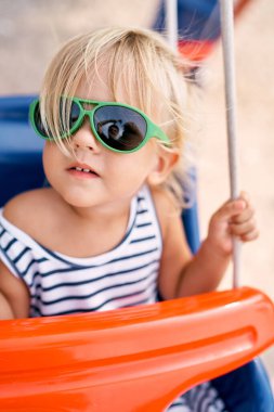 Güneş gözlüklü küçük kız salıncakta otururken poz veriyor. Yüksek kalite fotoğraf