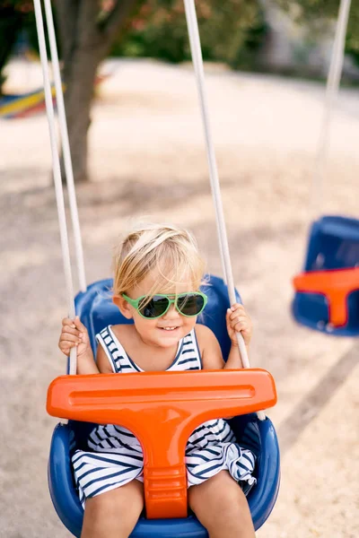 Güneş gözlüklü gülümseyen küçük kız salıncakta sallanıyor. Yüksek kalite fotoğraf