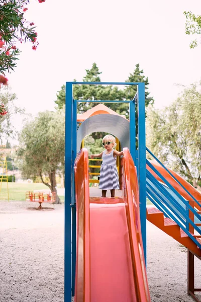 戴太阳镜的小女孩站在儿童滑梯上 高质量的照片 — 图库照片