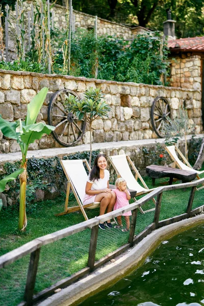 Anne ve küçük kızı göl kenarındaki katlanan sandalyelerde oturuyorlar. Yüksek kalite fotoğraf
