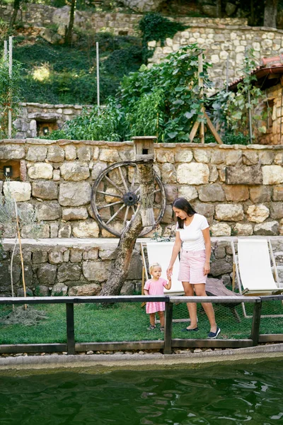 Annesiyle birlikte küçük bir kız gölün kenarında duruyor. Taş bir duvarın arkasında. Yüksek kalite fotoğraf