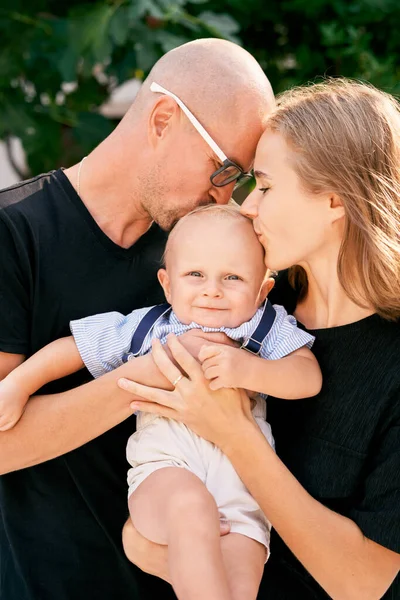 Happy mom and dad kiss a little boy from both sides. High quality photo