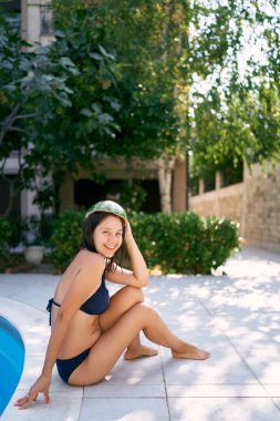 Kafasında karpuzla havuzun kenarında oturan gülümseyen kız. Yüksek kalite fotoğraf