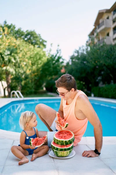 Baba ve küçük kız, yuvarlak parçalara ayrılmış karpuz yiyorlar. Yüksek kalite fotoğraf