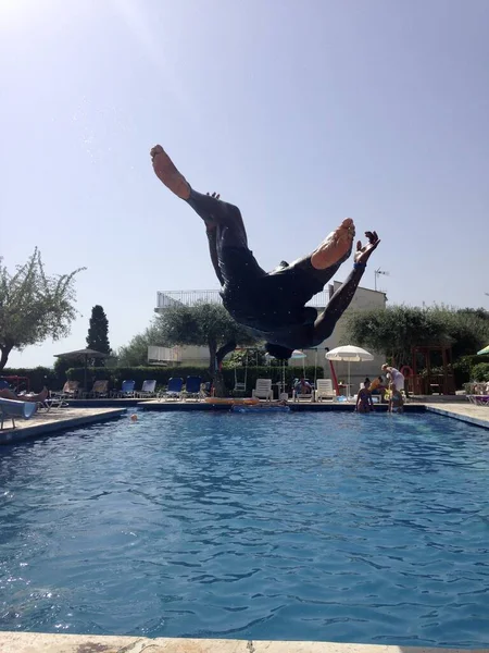 A man back-flipping into a hotel pool on a sunny holiday