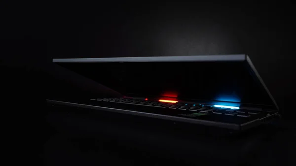 Gaming laptop closeup on black background illuminated by red and blue light from the back