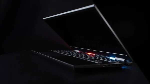 Gaming laptop closeup on black background illuminated by red and blue light from the back