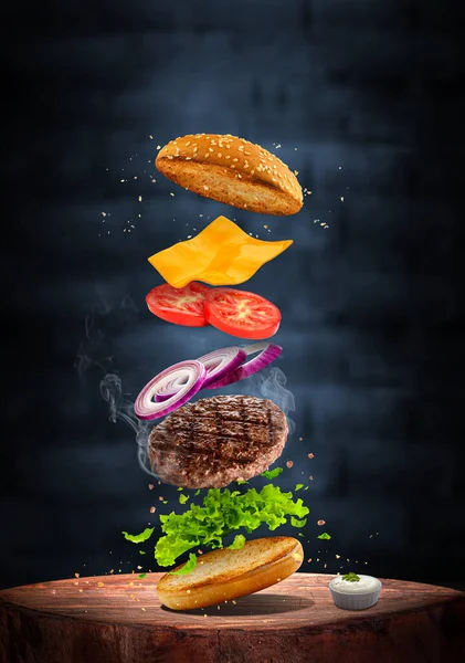 delicious grilled beef burger with flying ingredients isolated on dark background