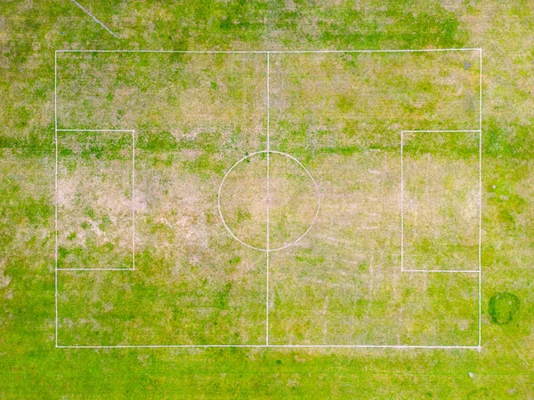 Aerial view of local football field during drought with patches of dry bare ground and green grass.