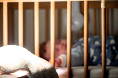 Yatak odasındaki loş ışık kaynağına odaklan, bebeğin arka plandaki beşiğinde uyumasına.