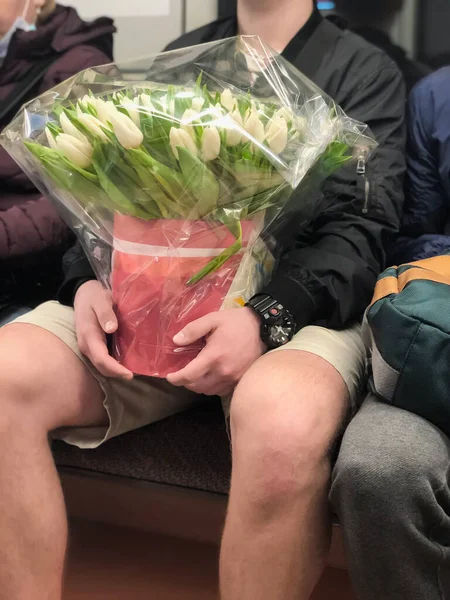 Gros plan d'un grand bouquet de tulipes blanches entre les mains d'un jeune homme dans le métro Image En Vente