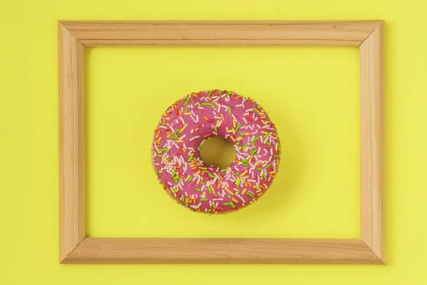 Donut acristalado brillante fresco en marco de madera sobre fondo amarillo, arte dulce abstracto inusual — Foto de Stock