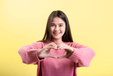 Güzel romantik bir kadın, sevgi ve sevgisini mutlu bir gülümsemeyle ifade etmek için işaret parmağıyla bir kalp hareketi yapar..