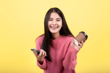 Elinde cep telefonu tutan mutlu Asyalı kadın elinde pembe arka planda bir fincan kahve tutarken mutlu bir yüz..