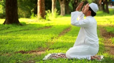 Young Asian Muslim man prostrating while offering prayer in a beautiful mosque on green meadow.