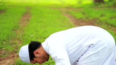 Young asian muslim man praying praying or performing Ssalah while sitting on Prayer rug and touching head to mihrab or mosque printed on rug