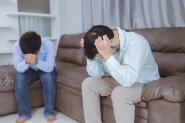 Genç bir çift evde oturmuş kafalarına dokunuyor.