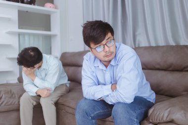 Genç Asyalı eşcinsel çift evdeki kanepede tartışıyor.