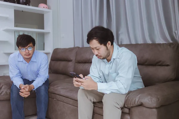 young man and older man using smartphone while sitting on sofa at home