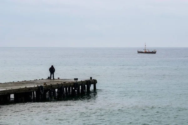 Одинокий Человек Пирсе Маленькая Яхта Вдалеке Облачную Погоду — стоковое фото