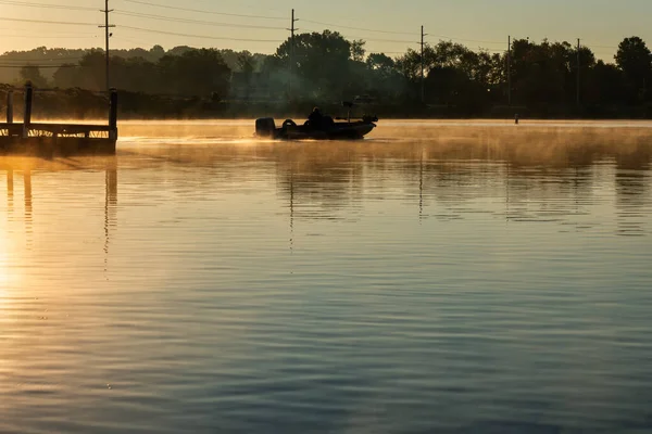 A man going bass fishing in a bass boat early morning sunrise on a foggy Time Ford Lake in Tennessee.