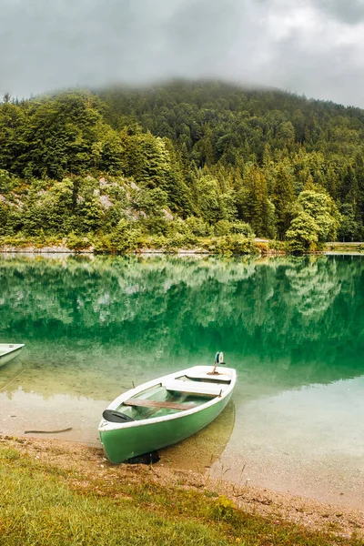 Morning on the lake in Bavarian Alps. Green boat near coast, clouds in mountains, Germany. Beautiful landscape with reflection in calm water. Outdoor relaxing photo.