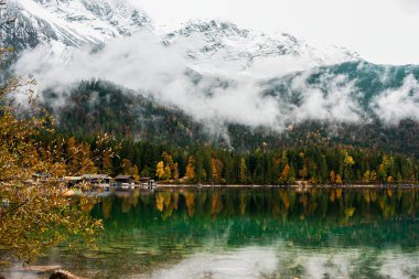 Cozy autumn morning in the Bavarian mountains, Germany. Alps landscape with lake coast, small village, clouds, forest and reflection in water. Outdoor beautiful photo. Wild nature.