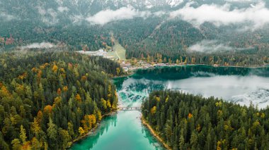 Autumn in the Bavarian mountains, Germany. Alps landscape with lake, bridge, clouds, forest, coast and turquoise water. View from above. Aerial drone outdoor photo.