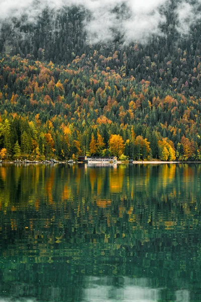 Cozy autumn morning in the Bavarian mountains, Germany. Alps landscape with lake coast, small village, clouds, forest and reflection in water. Outdoor beautiful photo. Wild nature.