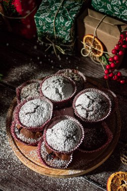 Powdered sugar muffins on wooden plate and Christmas gifts. New year boxes with kraft, red, green paper decoration. Still life close up. Food photo.