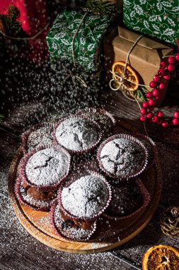 Powdered sugar muffins on wooden plate and Christmas gifts. New year boxes with kraft, red, green paper decoration. Still life close up. Food photo.