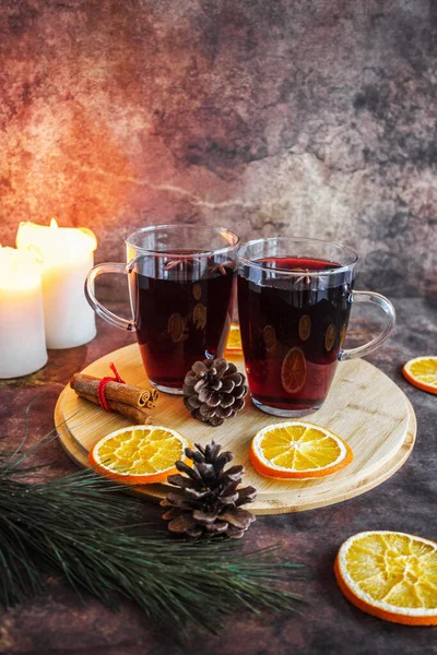 Two glasses with hot red mulled wine drink on the background of candles, dried oranges. Christmas still life. Hot winter beverage.