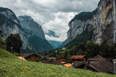 Lauterbrunnen valley, Switzerland. Swiss Alps. Cozy small village in mountains. Forest, rocks, clouds and green meadows. Beautiful landscape, Europe. Wooden houses, traditional chalet roofs.