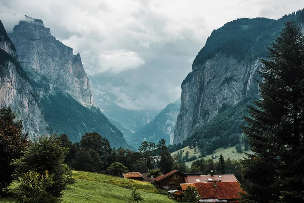 Lauterbrunnen valley, Switzerland. Swiss Alps. Cozy small village in mountains. Forest, rocks, clouds and green meadows. Beautiful landscape, Europe. Wooden houses, traditional chalet roofs.