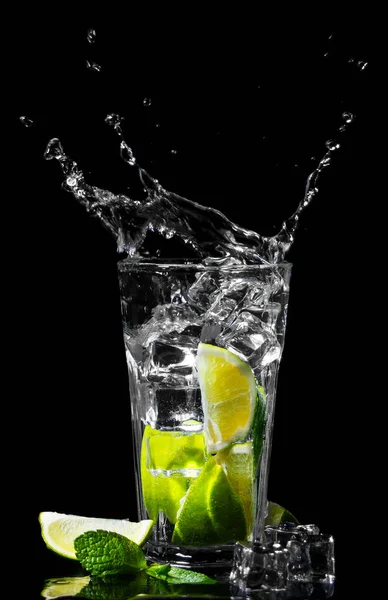 Splash water on the dark background. Mojito cocktail with lime, lemon, ice cubes and mint leaves. Drink glass. High quality photo