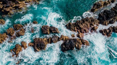 Stones among turquoise waves and sea foam from above. Atlantic ocean coastline with rocks. Madeira island, Portugal. Aerial drone photography. Beautiful landscape. Scenery outdoor background.