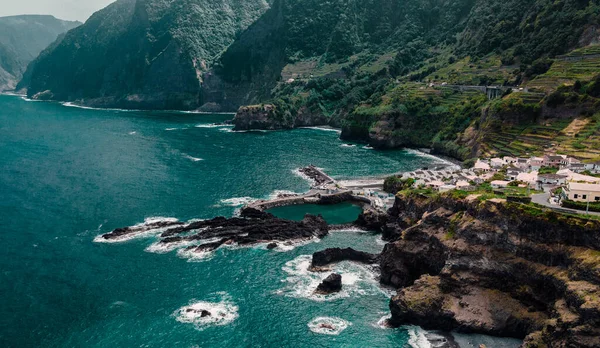 Natural swimming pools and small city on cliff, Atlantic ocean coastline. Madeira island, Portugal. Aerial photography from drone. Beautiful panoramic landscape.