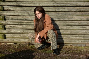 Young girl crouches on the floor in front of old wooden planks, looks down