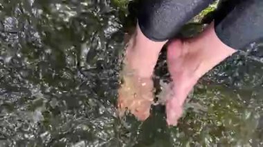 Kız ayaklarını dağ nehrine koydu. Hızlı akan bir nehirde kadınların ayakları.