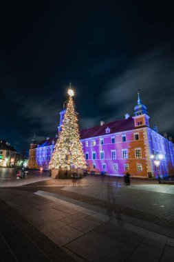 20.12.2021 Varşova. Kraliyet Kalesi 'nin önündeki kalenin tepesinde farklı renklerde ışıklandırılmış dev bir yıldızın olduğu bir Noel ağacı. Noel Uygulaması.